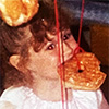 a toddler wearing a princess dress and crown eating a donut hanging from a string