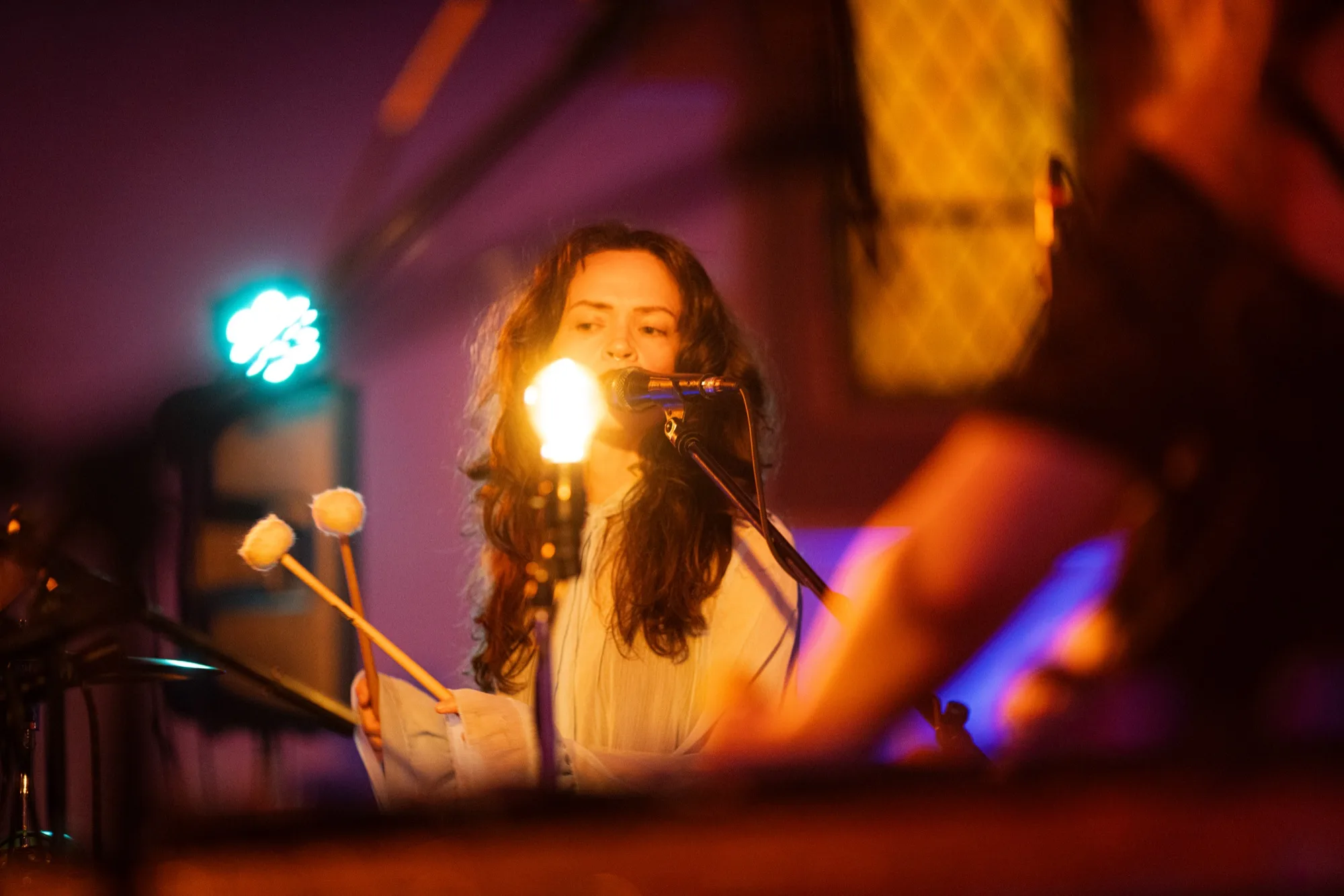 Close-up of me playing mallets on a vibraphone and singing into a mic, lit by a small lamp in a purple room.