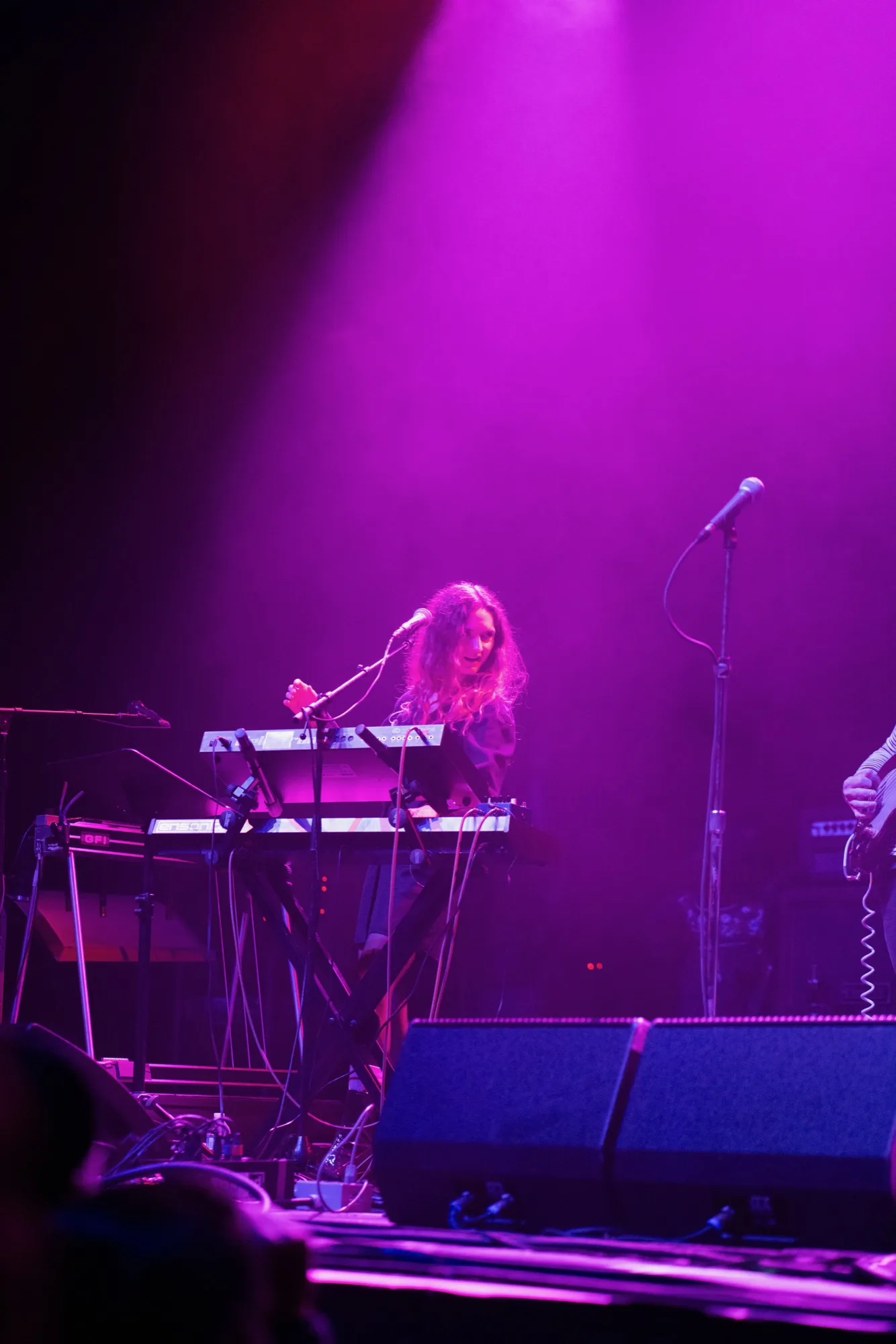 Distant wide shot of me playing keyboard alone on a big stage, bathed in purple light with the audience in silhouette.