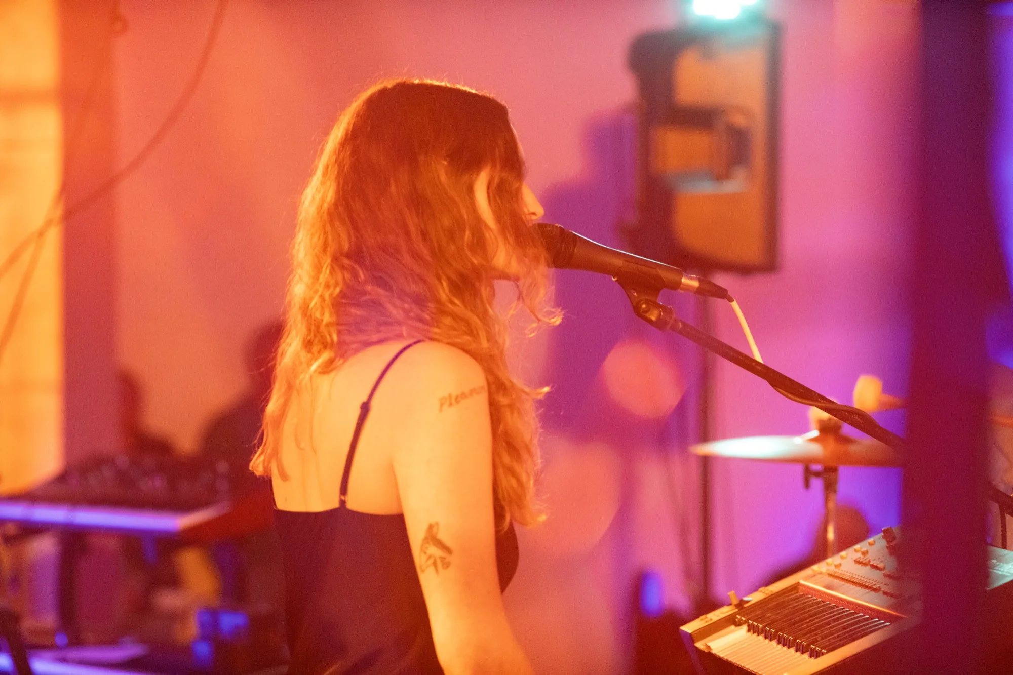 Me singing into a mic in profile, a tattoo visible on my arm, under purple stage light.